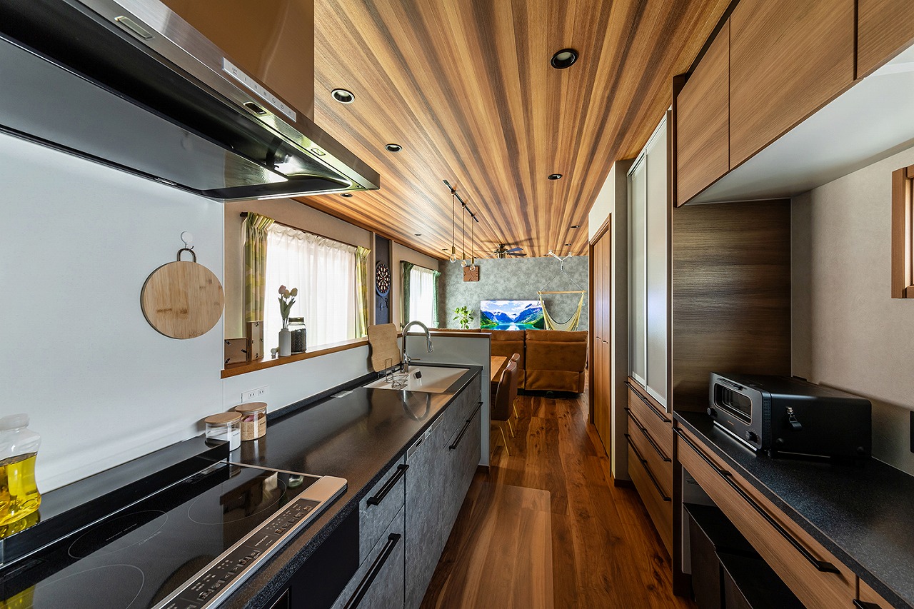 素材感のあるグレーのキッチンは、天板やキッチン家電を黒で統一し、カッコよさと高級感を感じる仕上がりに。木目のキッチンボードがリビングやダイニングともマッチし、調和のとれた空間を演出してくれます。