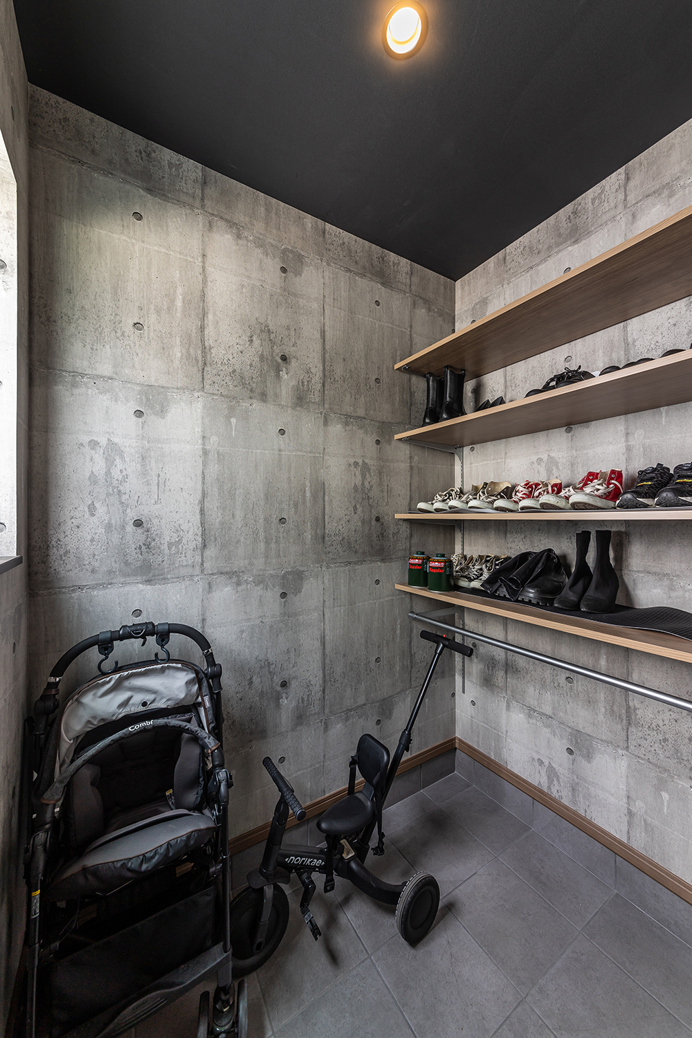 コンクリート調の壁紙が目を惹く玄関。<br />
玄関奥にある土間収納には、ベビーカーや三輪車の他、可動棚やハンガーパイプを利用し、靴や小物もたっぷりと収納できます。<br />
