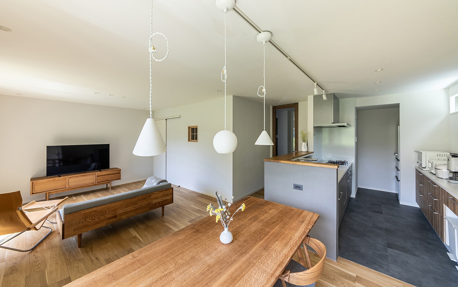 キッチンと横並びに配置したダイニング。<br />
家事動線が短く、効率的に料理の配膳や片付けが行える人気のレイアウトです。<br />
3灯連なる白いペンダントライトと木製のダイニングセットが北欧風のダイニングにピッタリです。