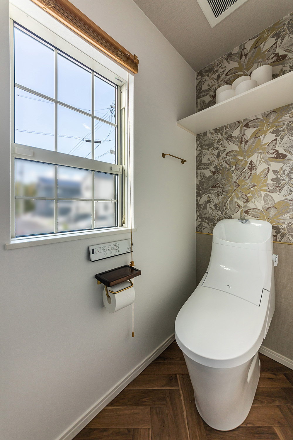 ヘリンボーン柄の床とボタニカル柄のアクセントクロスが目を惹くトイレ。<br />
上げ下げ窓から差し込む優しい光が、開放的な雰囲気を演出してくれます