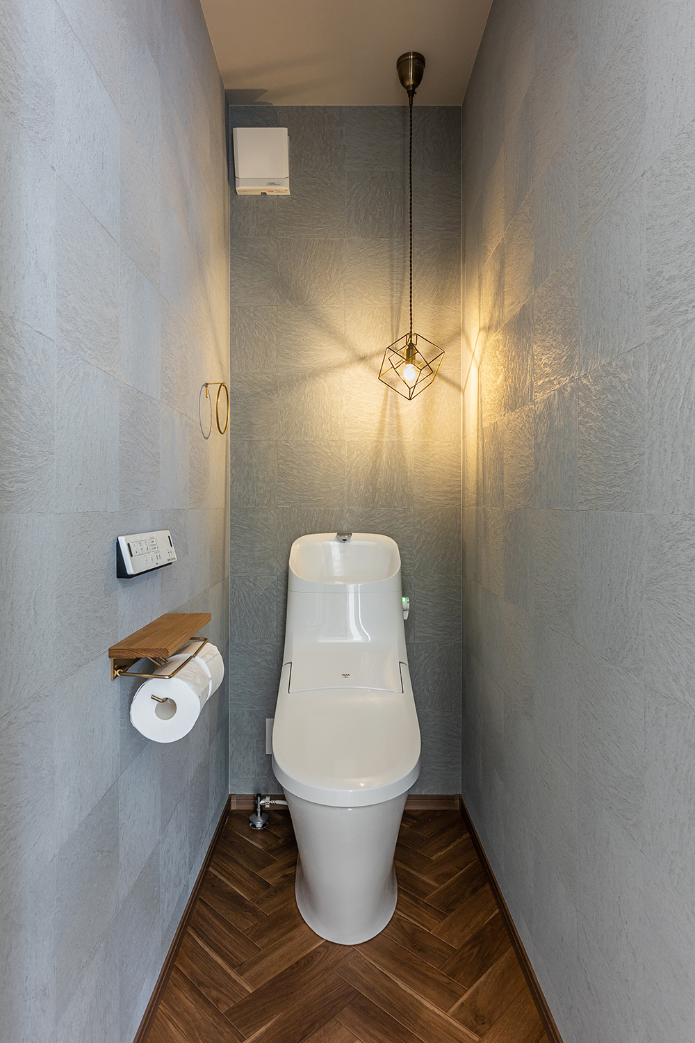 幾何学模様のペンダントライトがひと際目を惹くトイレ。<br />
グレーのクロスとヘリンボーン床がおしゃれに調和しています。