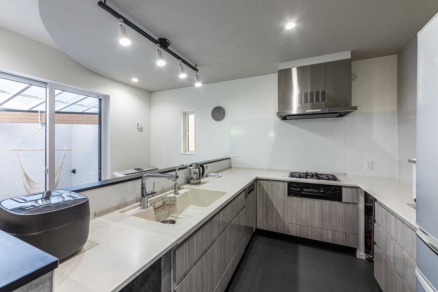 素材感のあるグレーのキッチン腰壁と木目調のキッチンが上品に調和。<br />
ダークグレーのフロアタイルとスタイリッシュなダクトレールライトが、空間にモダンで都会的な雰囲気を与えます。<br />
また、U型にキッチンを設置したことで、広いスペースで調理ができる空間に仕上げました。