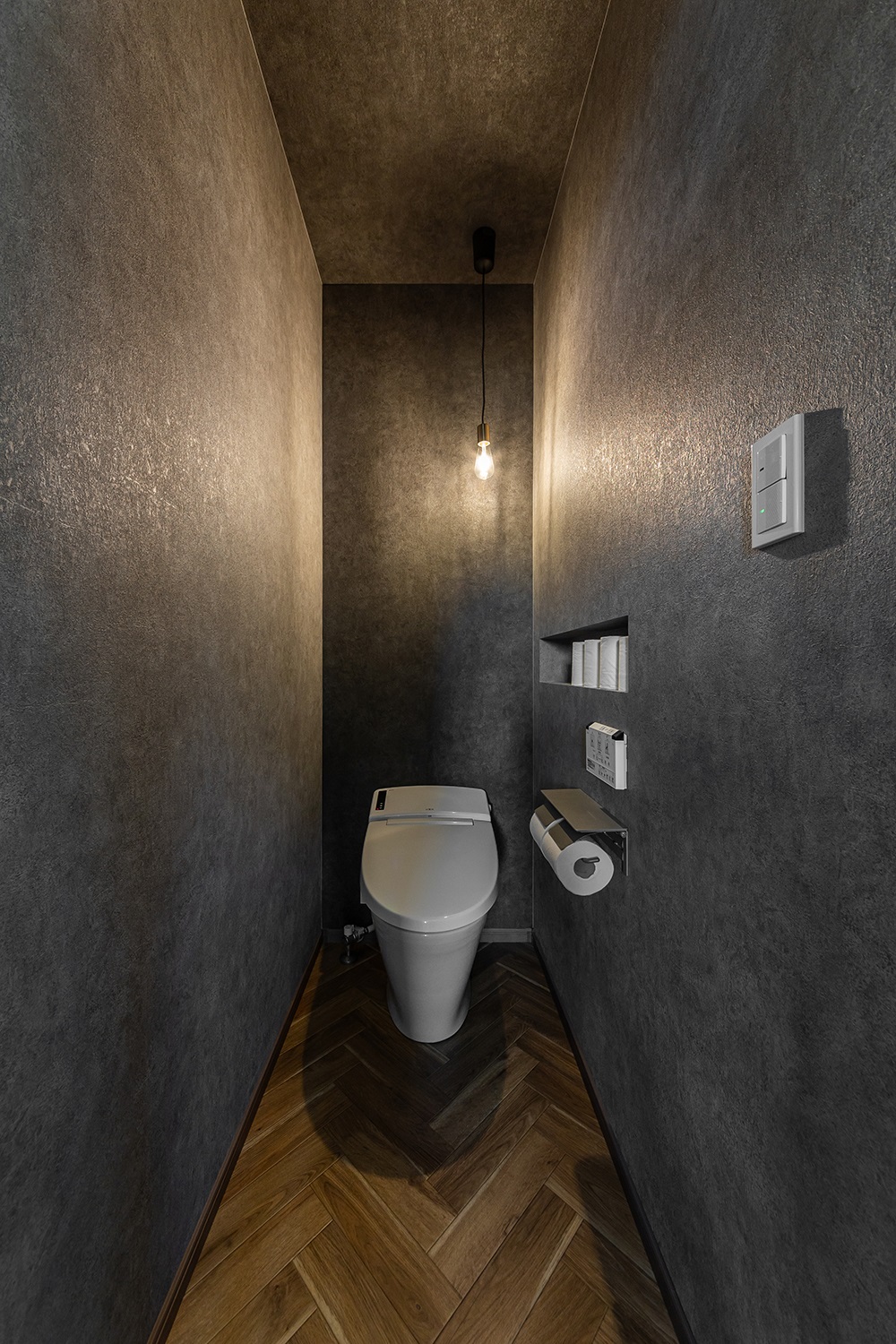 ヘリンボーン床にコンクリート調のクロスを合わせたオシャレなトイレ。<br />
落ち着いた空間にペンダントライトの柔らかな光が優しく灯ります。