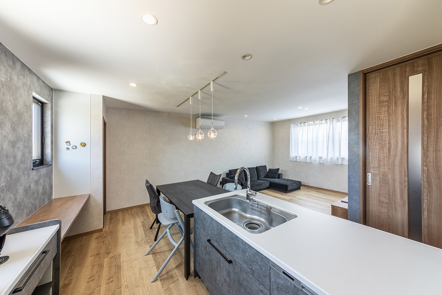 真っ白な天板が美しいグレーのキッチン。<br />
カウンタータイプのカップボードは開放感があり、カウンター上に家電を並べたりと見せる収納としても活用できます。<br />
ムラのある質感表現が美しいアクセントクロスと合わせ、洗練された上質な空間に仕上げました。