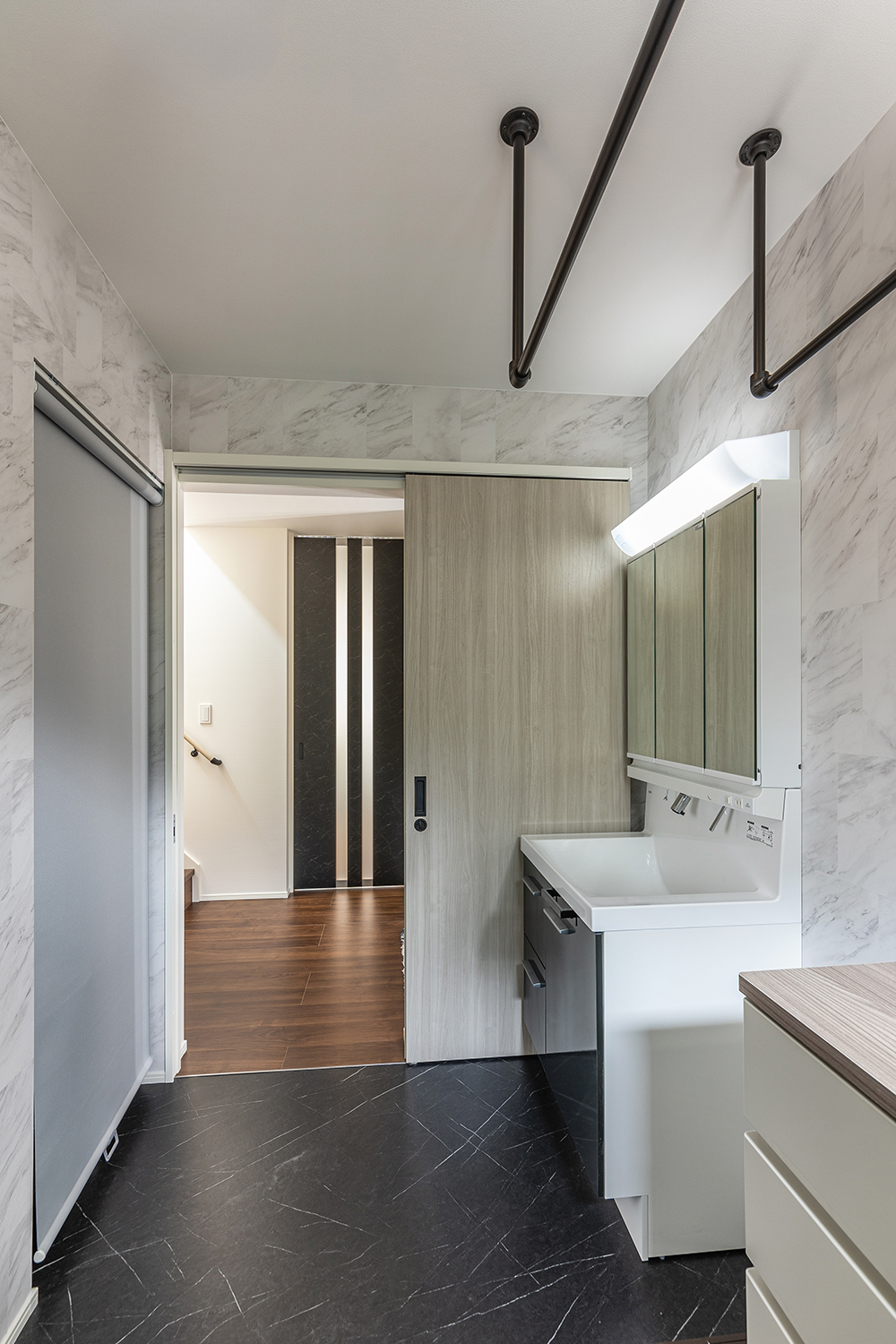 大理石調の壁紙が洗練された高級感を演出する洗面脱衣室。<br />
ハンガーパイプとランドリーチェストが完備されているため、洗濯の一連の作業がこのスペース一つでスムーズに完結することができます。