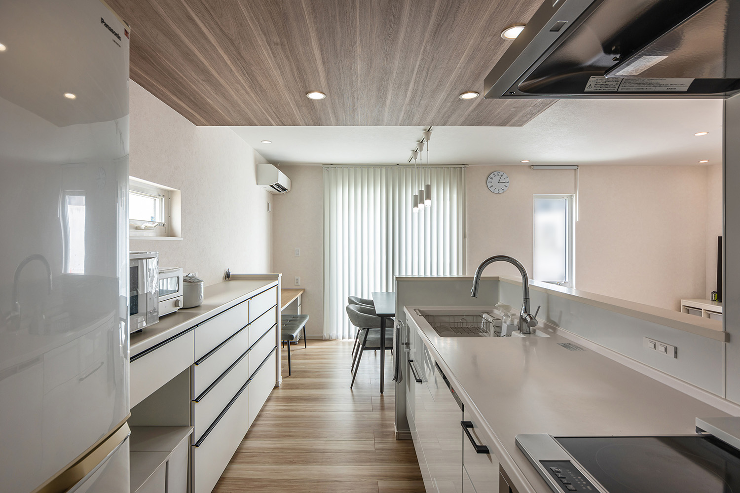 白で統一された清潔感あふれるキッチンは、青色のアクセントクロスとの組み合わせで、空間に心地よい遊び心をプラス。<br />
さらに、木目調の折り下げ天井を設け、スタイリッシュながらも温かみを感じる場所に仕上がりました。