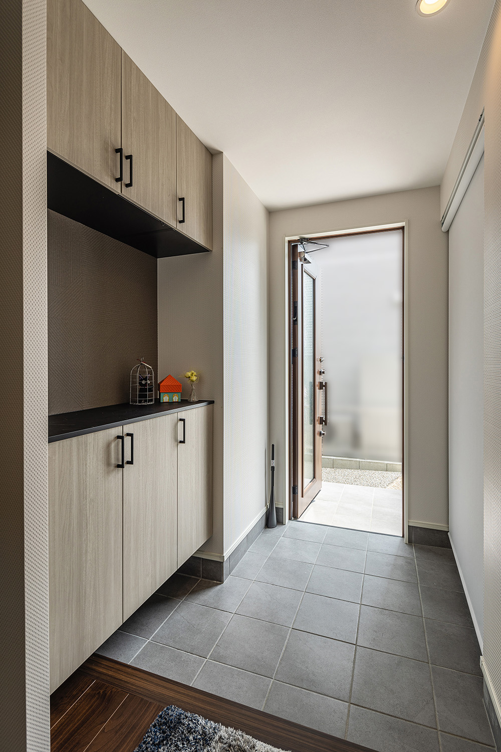 セメント特有のソリッドな質感のタイルと、白色のナチュラルな木目調の組み合わせが柔らかな印象の玄関。<br />
大容量収納することのできる、機能性もデザイン性も叶えたこだわりの玄関です。