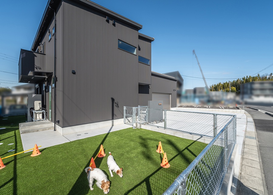 黒いガルバリウム鋼板に、片流れ屋根を組み合わせたスタイリッシュな外観。正面からはガレージに収まる2台の愛車が顔を覗かせます。<br />
庭一面には鮮やかな人工芝を敷き詰め、愛犬が思いきり走り回れる広々としたスペースを確保しました。