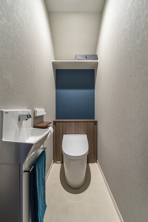 トイレはタンクレスタイプを選択し、すっきりとした空間に仕上げました。<br />
深みのあるネイビーのアクセントクロスが、空間に上質な落ち着きをもたらします。手洗いと収納も完備し、美しさと機能性を両立させました。